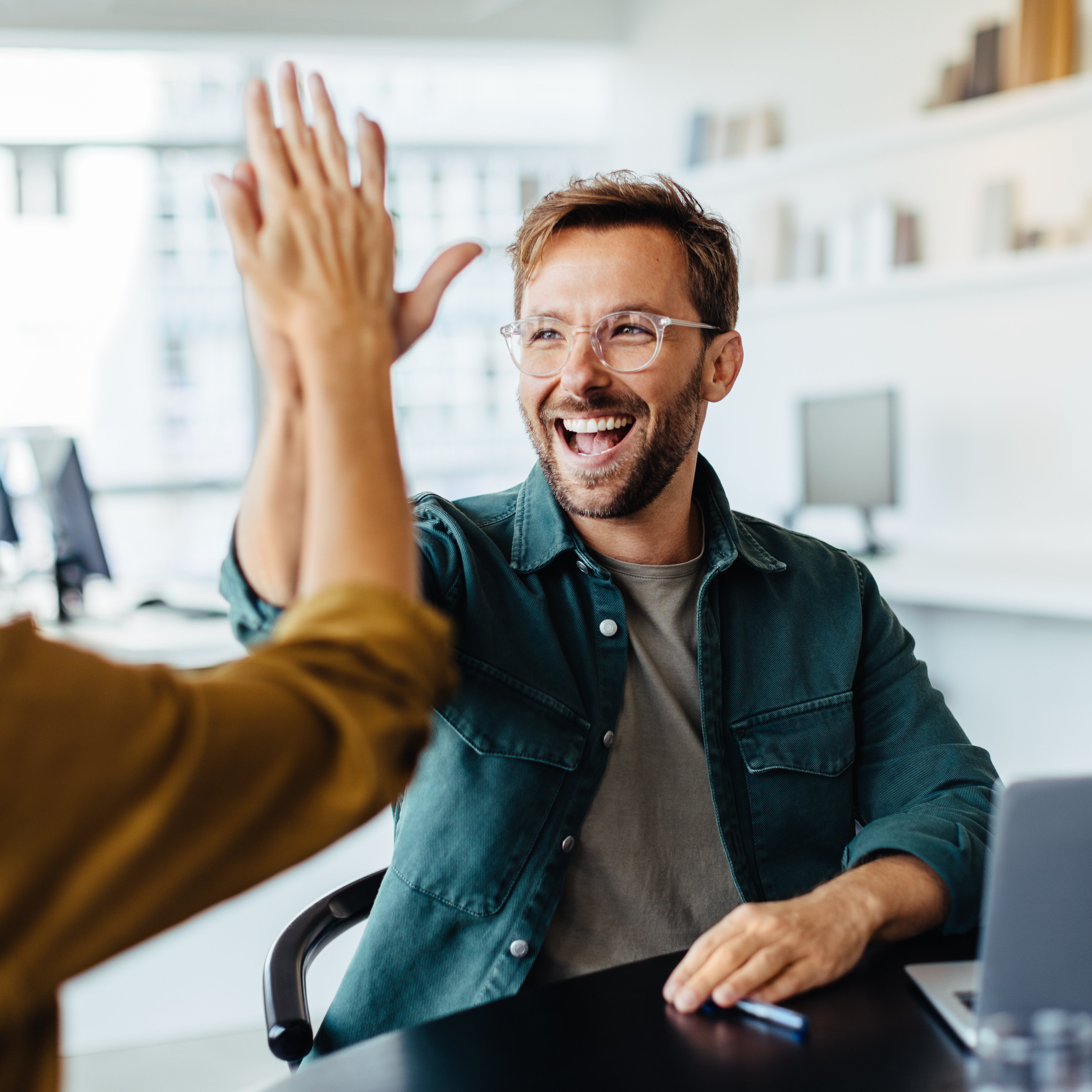 Successful business people giving each other a high five in a meeting. Two young business professionals celebrating teamwork in an office.